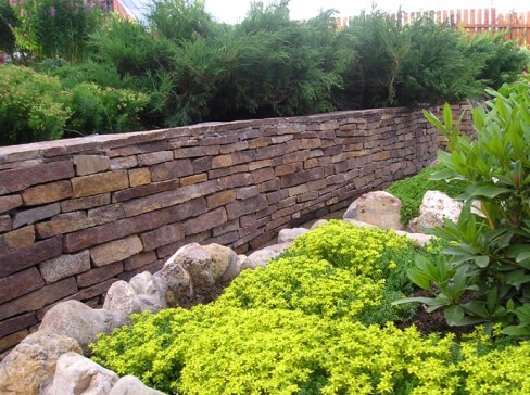 Muro de contención de bricolaje en un jardín de piedra, hormigón y madera